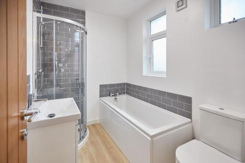 a bathroom with a tub and a toilet and a sink at Elfleda Stay - Modern 5 bedroom house with parking in Cambridge