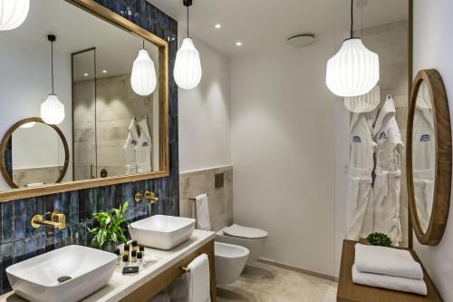 baño con lavabo, aseo y 2 espejos en Club Hotel Baja Sardinia, en Baja Sardinia