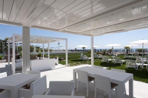 a patio with white tables and chairs and a lawn at Hotel Le Soleil in Lido di Jesolo
