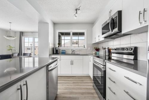 una cocina con armarios blancos y electrodomésticos de acero inoxidable en New Cozy Family Townhome Sleeps 10 Comfortably w Banff Pass, en Airdrie