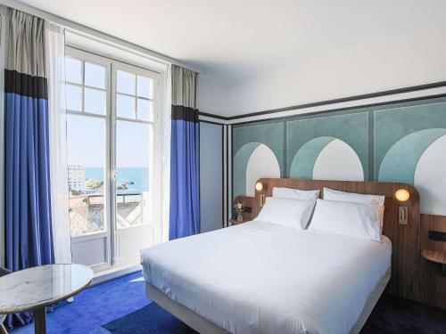 a bedroom with a bed and a large window at Mercure Plaza Biarritz Centre in Biarritz
