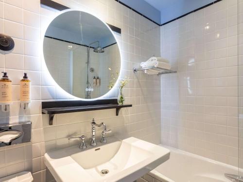 La salle de bains blanche est pourvue d'un lavabo et d'un miroir. dans l'établissement Mercure Plaza Biarritz Centre, à Biarritz