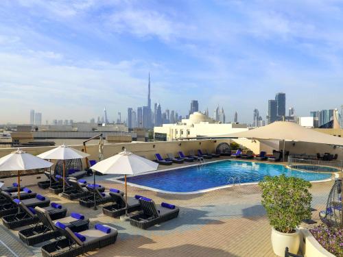 Mövenpick Hotel & Apartments Bur Dubai في دبي: مسبح فيه كراسي ومظلات على مبنى