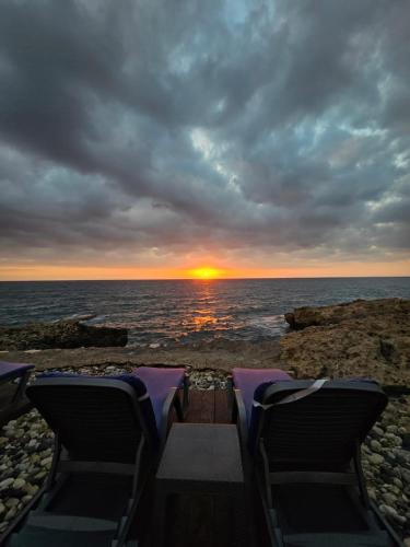 two chairs on a beach with a sunset in the background at Golden Stone Beach in Halat Byblos