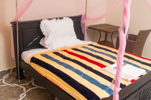 Una cama con una manta de rayas de colores y una mesa en Buvuma Island Beach Hotel en Jinja