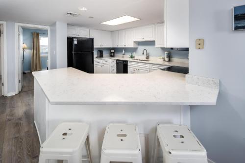 una cocina con armarios blancos y una barra con 3 taburetes en Nautilus 2609 Gulf View 2 Bedroom 6th Floor Free Beach Service en Fort Walton Beach