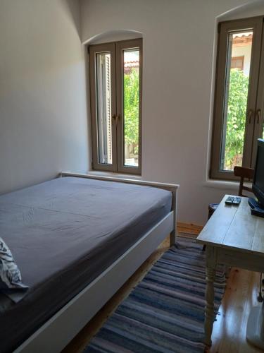 a bedroom with a bed and a desk and two windows at Vagia's Home in Kymi