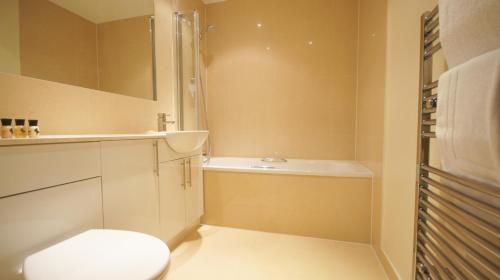 a bathroom with a toilet and a tub and a sink at Crompton Court Apartments in London