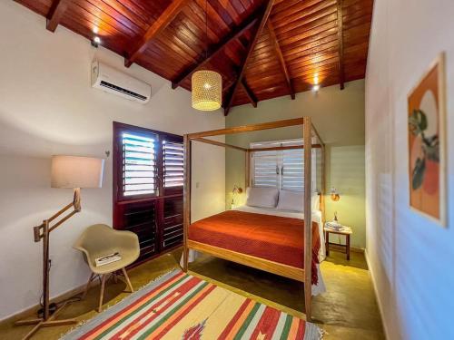 um quarto com uma cama, uma cadeira e uma janela em Casa Sapoti - 3 Suítes no centro em Pipa