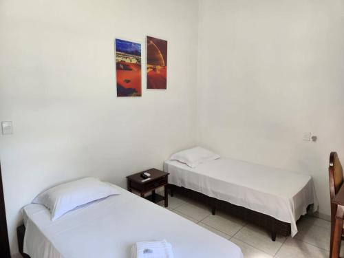 a room with two beds and a table and a picture at Hotel Colonial in Cajati