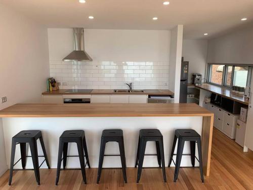 a kitchen with a large counter with four bar stools at Three Little Birds at Freycinet in Coles Bay