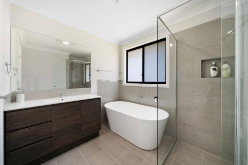 a bathroom with a tub and a sink and a mirror at Relaxing Two-Level Retreat in Austral, NSW in Austral