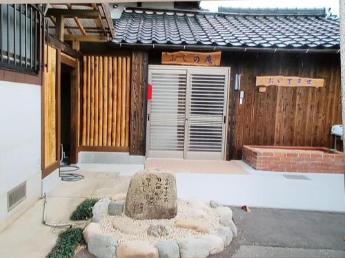 una casa con una estatua de piedra delante de ella en ゲストハウス ふしの庵 en Ogori
