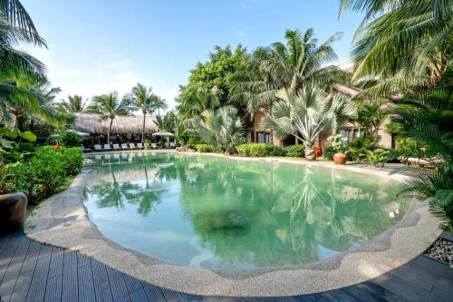 a swimming pool in front of a resort with palm trees at M Village Phu Quoc in Phu Quoc