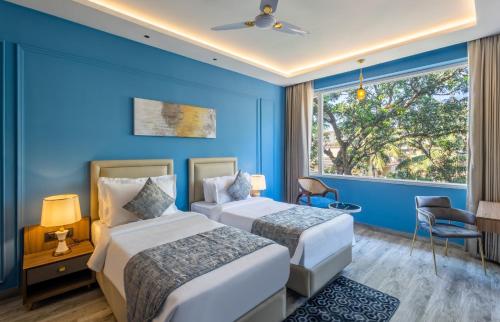 Renest Calangute Goa في كالانغيُت: سريرين في غرفة زرقاء مع نافذة