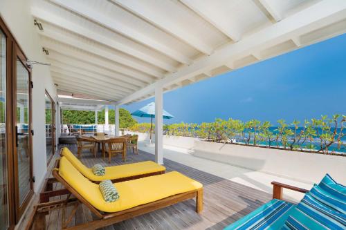 a porch with a yellow couch and a table and chairs at OBLU NATURE Helengeli-All-Inclusive with free Transfers in North Male Atoll