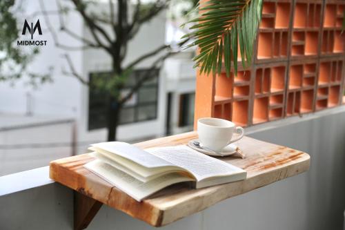 um livro e uma chávena de café numa mesa de madeira em MIDMOST CASA em Can Tho