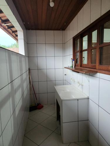 baño de azulejos blancos con lavabo y ventana en Hospedagem Vanilda, en Nova Friburgo