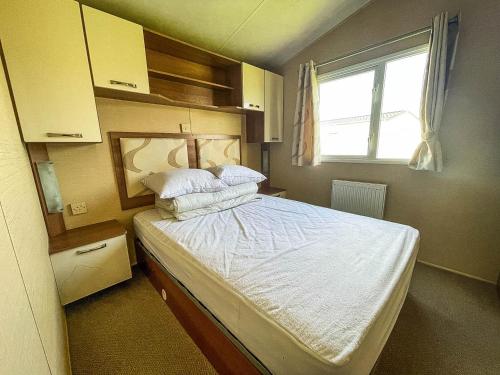 Schlafzimmer mit einem Bett mit weißer Bettwäsche und einem Fenster in der Unterkunft Modern Caravan With Wifi At Martello Beach Holiday Park In Essex Ref 29010kv in Clacton-on-Sea