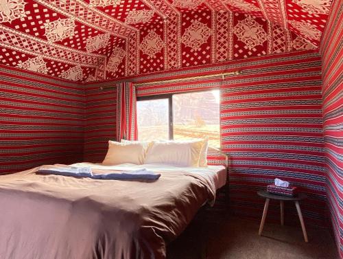 Ce lit se trouve dans un dortoir doté d'un mur rouge et noir. dans l'établissement Bedouin Yoga & Trekking Camp Wadi Rum, à Wadi Rum