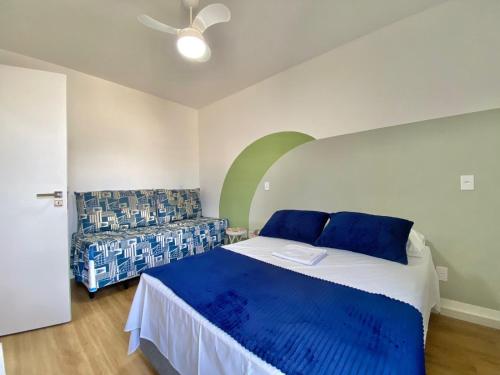 una camera da letto con un letto con cuscini blu e un divano di FLAT COM VARANDA E SERVIÇOS NO RIVIERA GREEN a Bertioga