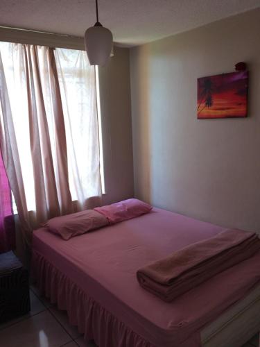 a bed in a room with a window with pink sheets at Kingswood Flats in Pretoria