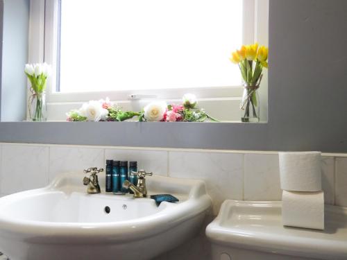 a bathroom with a sink and flowers in a window at Tudors eSuites Four Bedroom House + Garden in Coventry
