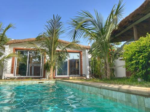 a swimming pool in front of a house with palm trees at Keur Ama in Mbour