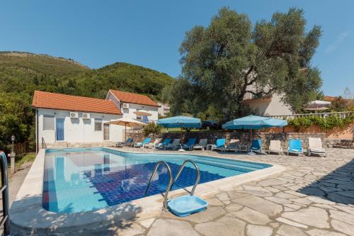 a pool with chairs and umbrellas next to a house at Villa Mia Apartments in Bijela