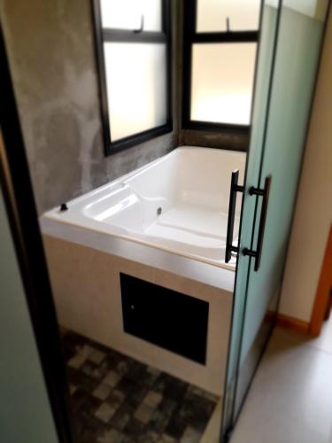 a bath tub in a bathroom with two windows at Pousada Kirana in Praia do Rosa