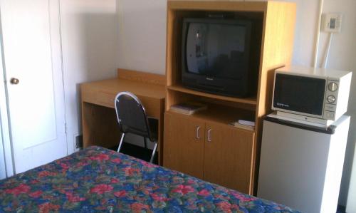 a room with a bed and a tv and a desk at San Joaquin Motel in Merced