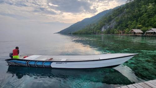 a man is sitting on a boat in the water at Terimakasih homestay in Pulau Mansuar