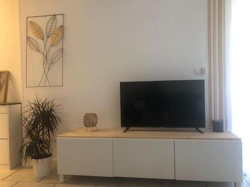 Elle comprend une télévision à écran plat installée au-dessus d'un meuble blanc. dans l'établissement Le Drakkar - Studio chaleureux *Parking *CLIM *Wifi 2 pers., à La Grande Motte