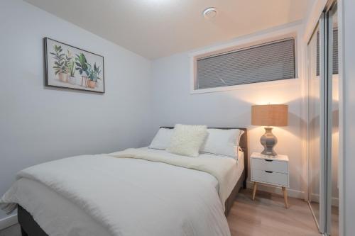 a white bedroom with a bed and a lamp at Serene Elegance 2BR Gem with modern conforts in Calgary