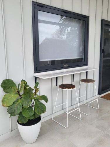 a tv on a stand with two stools and a plant at Coastal Pod in Port Macquarie