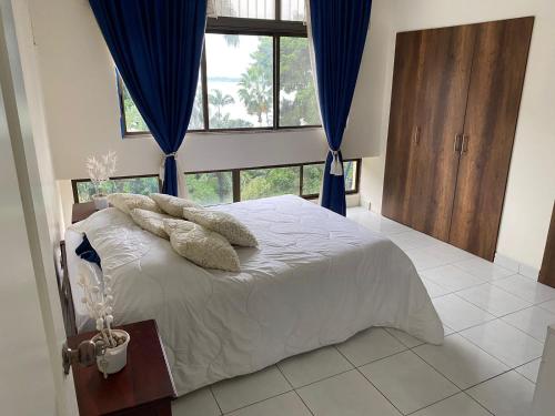 een slaapkamer met een wit bed met blauwe gordijnen en een raam bij Edificio Riviera in Guayaquil