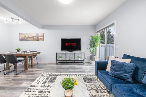 a living room with a blue couch and a table at Large Townhome Near Anthony Henday in Ellerslie with Driveway & Visitor Parking, King Bed, 4 Queen Beds, Fully Equipped Kitchen & More! in Edmonton