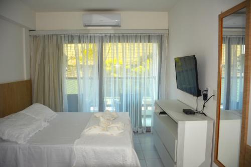 a bedroom with a bed and a tv and a window at Araça flat 308 - Lateral Vista Jardim in Natal