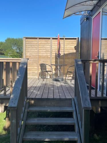 a deck with a table and chairs and an umbrella at Cotman Cottage on Coatesville in Kumeu