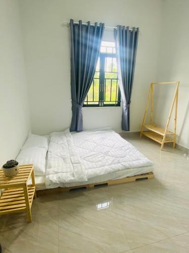 a bedroom with a bed and a window with blue curtains at Homestay Nhà Của Gạo in Bao Loc
