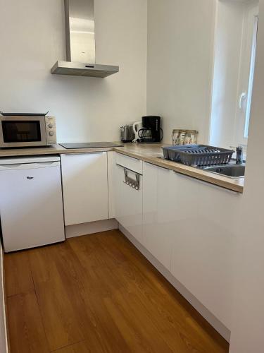 une cuisine blanche avec un évier et un micro-ondes dans l'établissement Dinan - appartement centre ville, à Dinan
