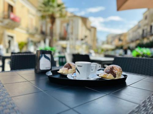 um prato com uma chávena de café e bolos sobre uma mesa em B&B - Piazza Grande em Gela