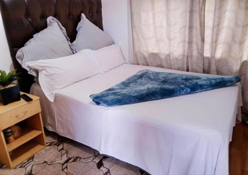 ein Bett mit weißer Bettwäsche und einer blauen Decke darauf in der Unterkunft NSK GUEST HOUSE in Alberton