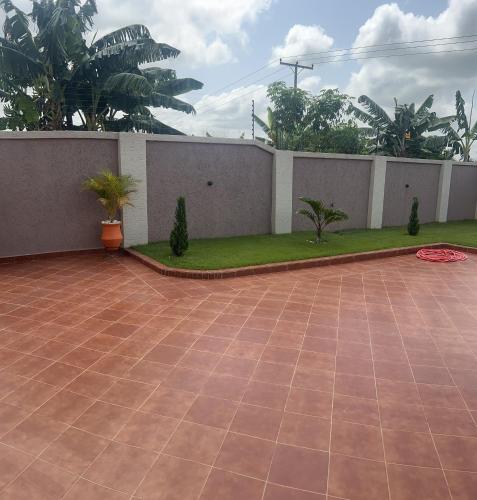 a patio with a wall and a yard with trees at Boulevard Court in Ejisu