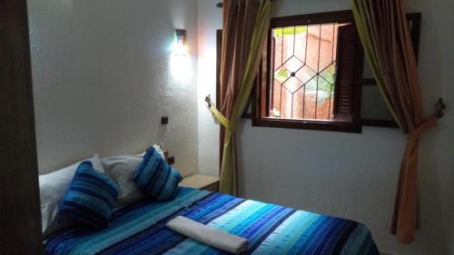 a bedroom with a bed with blue pillows and a window at Mirleft Tayought Guest House in Mirleft