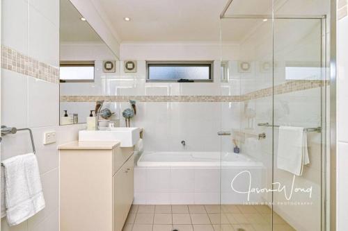 The Salty Seagull – ocean-view luxe! في Encounter Bay: حمام أبيض مع دش وحوض استحمام ومغسلة