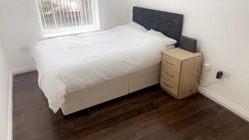 um quarto com uma cama branca e uma mesa de cabeceira em madeira em 2 bedroom apartment, free parking & WIFI near City Centre em Manchester