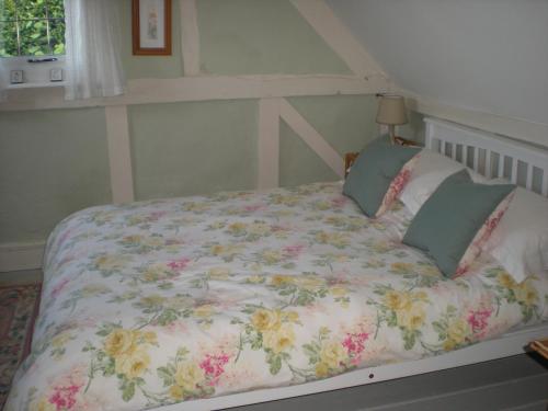 a bed with a floral comforter and two pillows at Hillside Cottage in Ledbury