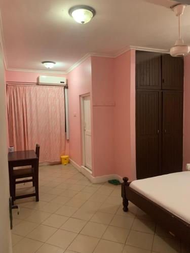 1 dormitorio con paredes rosas, 1 cama y escritorio en Kibodya Hotel Nkrumah, en Dar es Salaam