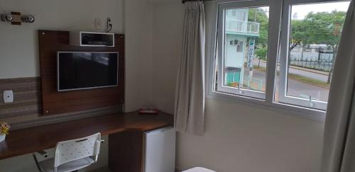 um quarto com uma secretária, uma televisão e uma janela em Hotel Boa Vista em Chapecó